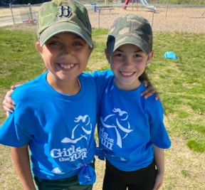 Two Girls on the Run participants in blue shirts smiling in hats